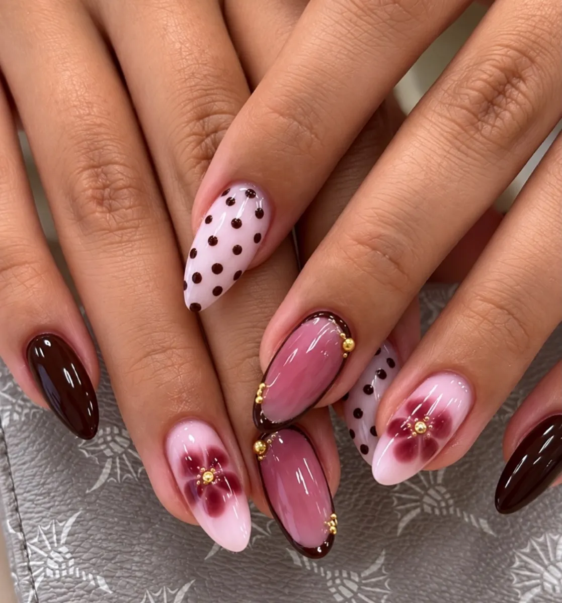 Mandelförmige Nägel in Schokobraun und Rosa mit gemalten Blüten, Punkten und goldenen Details